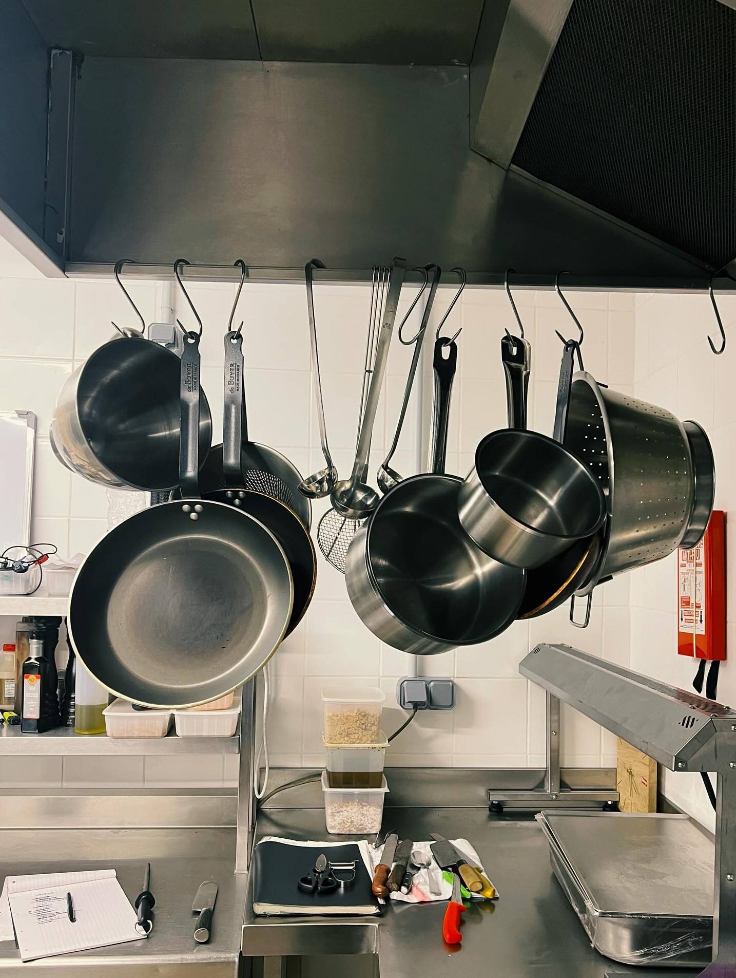 Casseroles et poêles suspendues au-dessus du plan de travail d’une cuisine professionnelle.