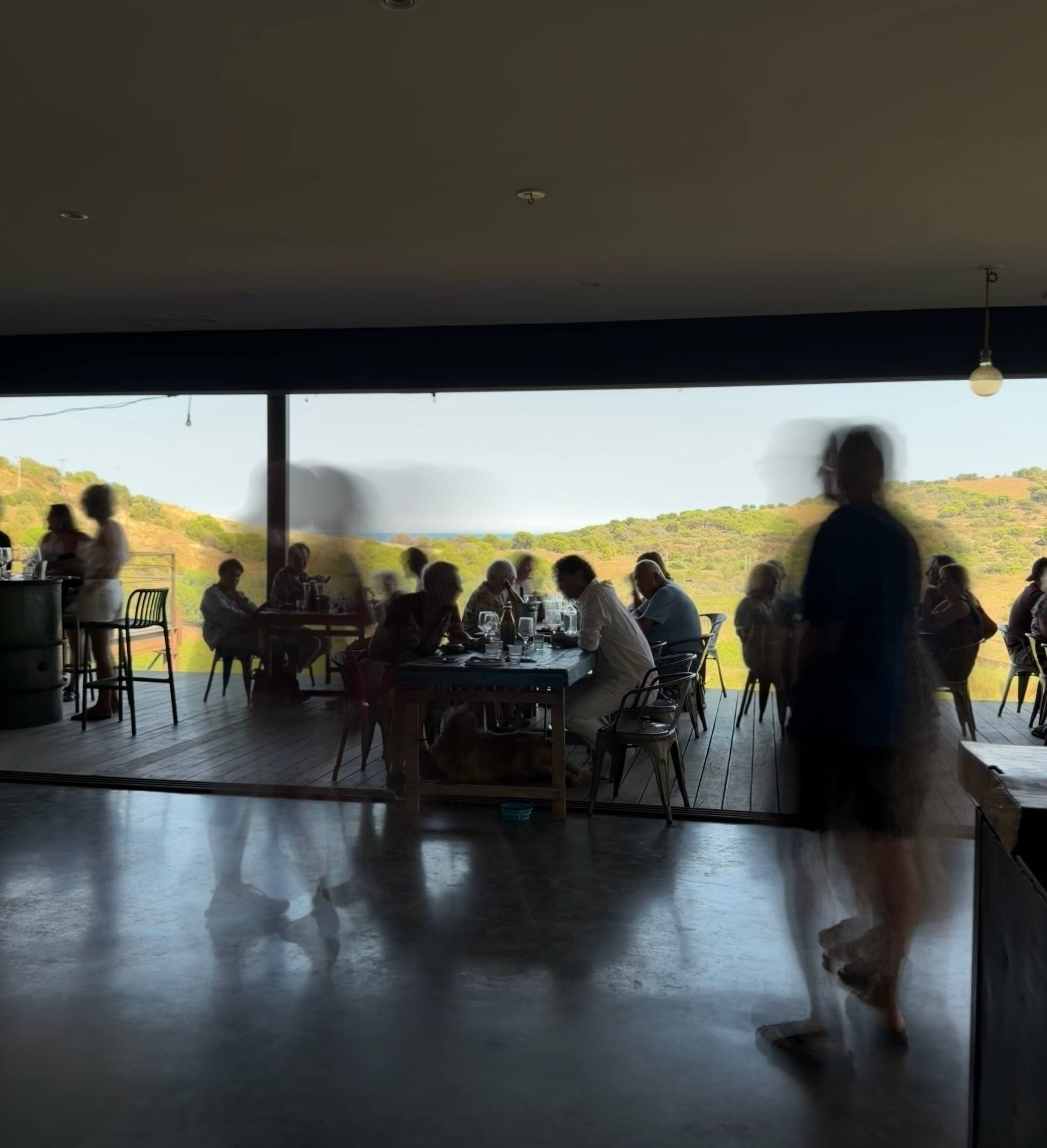 Convives attablés dans une salle ouverte sur les collines, chez Mémé Jeannette.