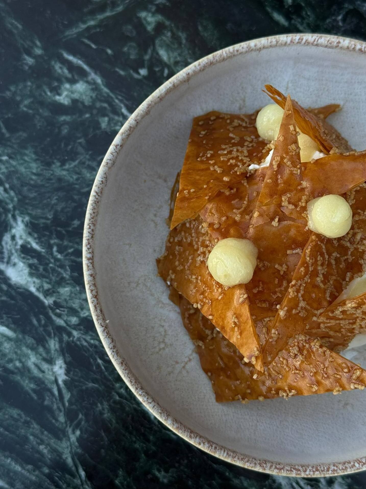 Gros plan sur le mille-feuille yuzu : tuiles caramélisées, pointes de crémeux, assiette claire sur marbre vert.