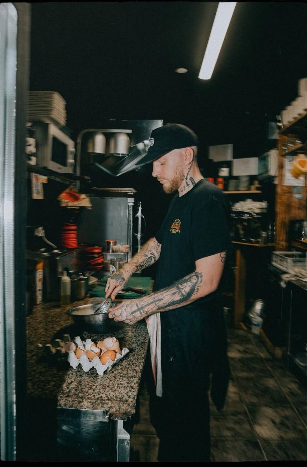 Le chef en casquette, fouet en main au-dessus d’un saladier, dans la cuisine du Repère.