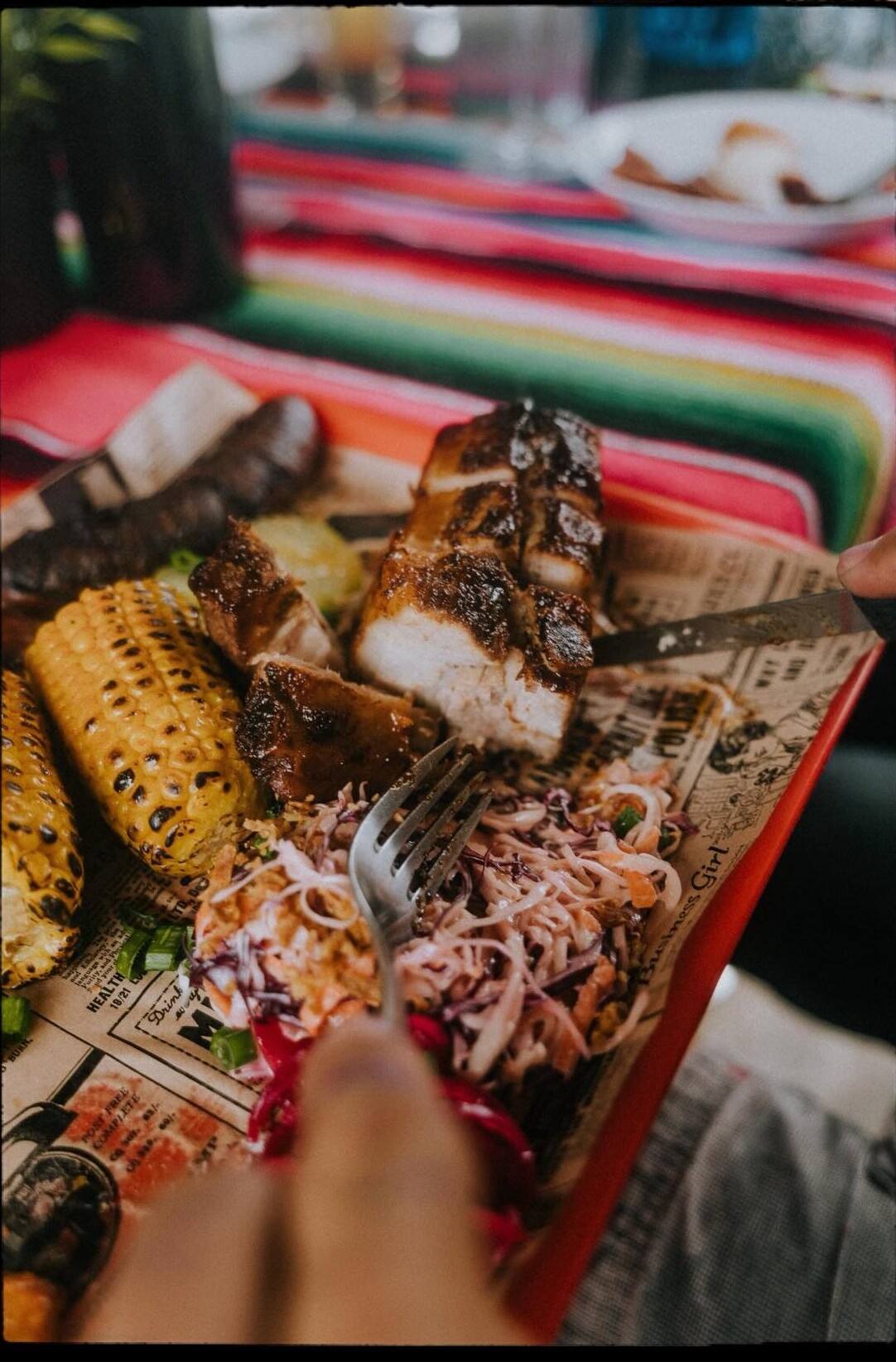 Une fourchette plantée dans une assiette à partager : maïs grillé, viande effilochée, chou.