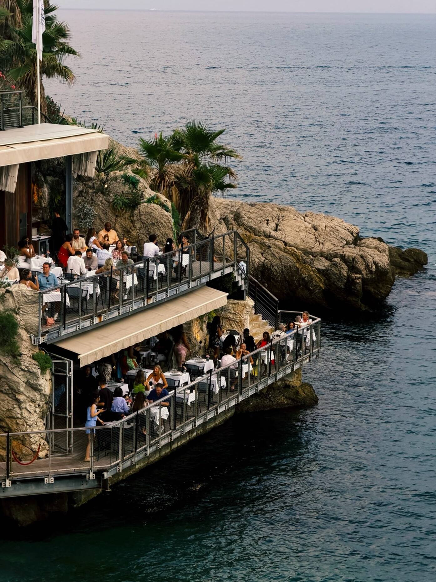 Une terrasse de restaurant accrochée aux rochers, au-dessus de la Méditerranée.